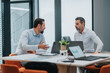 © qunica.com - Two colleagues engage in a focused discussion at a contemporary office, with laptops, charts, and a small plant on the table. The scene conveys collaboration, planning, and professional teamwork.