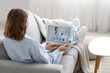 © Pixel-Shot - Diabetic young woman with glucometer and lancet pen talking to doctor online on sofa at home, back view