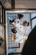 © qunica.com - A top-down view of a diverse team gathered around a white table, sharing colorful charts and documents in a bright, modern office. Collaboration, planning, and strategy in a casual business setting.