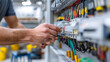© Alesia - A close-up of a male technician's hand working on electrical wiring in a control panel. Colorful wires and connectors are visible in the background.