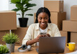 © md - Smiling young black woman working on laptop and phone surrounded by moving boxes