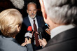 © Seventyfour - Middle aged Caucasian man speaking to group of journalists holding microphones during press conference, reporters interviewing and recording responses, news channel microphone visible