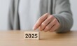 © K4VEE - Close-up of a hand pointing toward wooden blocks displaying the year 2025, representing future business planning, strategy, and goals.