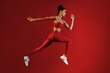© Prostock-studio - A young woman in red activewear sprints energetically, showcasing her athleticism. She leaps forward with determination, set against a striking red backdrop that enhances her movement.