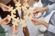 © Studio Romantic - Hands hold puzzle pieces symbolizing teamwork and connection. A diverse group aligns wooden pieces, showing support, unity, and strategy to find a solution. Metaphor of collaboration and unity.