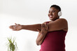 © Prostock-studio - Motivated young black woman with short hair stretches her arms at home. She wears a wireless headset and smiles while enjoying her music during exercise.