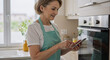 © Running opossum - mature caucasian woman using smartphone in a modern kitchen with a cheerful expression
