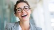 © mila103 - A young woman with glasses is smiling joyfully while sitting in a contemporary office. Her cheerful expression radiates happiness creating a positive atmosphere.