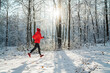 © Soloviova Liudmyla - Trail runner woman dressed bright red windproof jacket jogging picturesque snowy forest path during sunny frosty day. Sporty active people and winter training concept image.