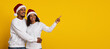 © Prostock-studio - Two smiling individuals wear Santa hats and embrace joyfully. They stand against a vibrant yellow background, with one pointing excitedly. The scene captures holiday cheer and warmth.