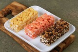 Three colorful sachima blocks arranged on a wooden tray. Bright, clean food image for snack or dessert themes.