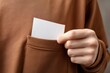 © SilentSmog - close-up of a hand taking out a white sticker with an empty space for text from a brown sweatshirt pocket. this is a mockup template of a blank label inside a sleeve, shown in close-up.