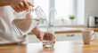 © AucArtStudio - Person pouring clean water from glass pitcher into drinking glass on kitchen counter promoting easy access to hydration and calm everyday moment