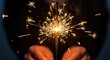© Shehnaz - Close up of hands holding a sparkler with bright light and dark background