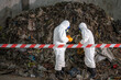 © BESTIMAGE - Two forensic investigators in protective suits collecting evidence at a large outdoor landfill site with piles of trash and waste, environmental cleanup and pollution control scene