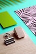 © Nisa - A close-up, overhead shot features office supplies arranged on a bright turquoise surface, including a binder clip, a small wooden block, a green card, and a pi