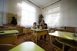 © Niko_Dali - Teacher and young student in classroom. The pair sit at desks under bright windows in the well lit educational space.