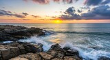 Vibrant sunset illuminates rocky coastline with powerful ocean waves crashing against the shore