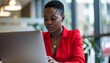 © Roberto - a black business woman with short hair wearing a red blouse top focusing intensely on her laptop computer in the office