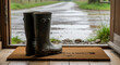 © val_webart - Rubber boots on welcome mat by open door on rainy day