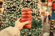 © EdNurg - Person holding a chimney cake street food while visiting festive Christmas market decorated with a large nutcracker and sparkling tree