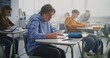 © Framestock - Young Boy Concentrates on Writing Task in Class. Other Students Working at Desks. Concept Student Focus, Academic Concentration, Process of Independent Work in Modern School Setting. Static Shot.