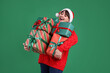 © New Africa - Smiling woman in Santa hat with many gift boxes on green background. Christmas and New Year celebration