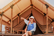 © EdNurg - Young woman pointing finger to something interesting while enjoying her glamping vacation in a luxury tent