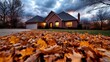 © Raul - Fallen leaves cover the driveway of a brick house during a cloudy dusk, showcasing autumnal colors and a cozy, residential scene.