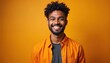 © Vadym - Young Indian man smiles brightly in studio. He wears casual orange shirt over gray t-shirt. Attractive guy with curly hair and beard has positive expression. Portrait of happy person.