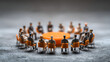 © utaem2022 - Miniature figures in a round table discussion with orange chairs and a central circular table