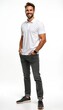 © Vadym - Young man in white polo shirt and grey trousers stands with hands in pockets. He smiles confidently at the camera in a studio. His casual yet smart attire suits many settings.
