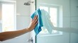© Leonardo - Una mano sujeta la mampara de la ducha y la limpia con un paño de microfibra azul vibrante, en un baño luminoso y ventilado