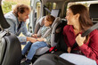 © Stockphotodirectors - A man and woman happily assist their young child in adjusting the car seat while preparing for a family outing. The sunny day suggests a fun trip ahead.