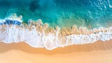 Overhead view of ocean waves crashing on a sandy beach, showing hues of blue, turquoise, and golden sand
