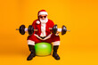 © deagreez - Santa lifts weights in a bright orange studio wearing red suit and hat on a green ball for a festive christmas fitness themed image