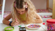 © khmelev - girl focused on arts and crafts using colorful beads with smartphone nearby. creative indoor hobby activity, promoting fine motor skills and concentration in playful environment