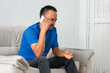 © Mauricio Toro - Side view of Latino man on sofa using phone, attentive, left hand missing four fingers visible to camera