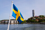 Swedish flag with colony of small wooden historic houses on the Slottsberget mountain with the tallest Scandinavian building Karlatornet skycraper in Lindholmen in background, Gothenburg, Sweden