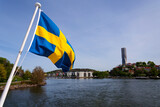 Swedish flag with colony of small wooden historic houses on the Slottsberget mountain with the tallest Scandinavian building Karlatornet skycraper in Lindholmen in background, Gothenburg, Sweden