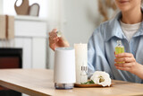 Woman with eustoma flower and candle adding essential oil to air humidifier on table in room, closeup