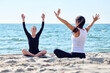 © TRAVELARIUM - Adult women practicing yoga with raised arms on Baltic Sea sandy beach under clear sky