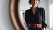 © SolaruS - Elegant woman looks at her reflection in a round mirror, wearing a stylish black dress with a brown belt. Great for fashion, beauty, and lifestyle concepts.