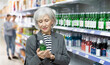 © JackF - Interested elderly woman carefully examining labels on bottles in Asian store, contemplating choice of soju, traditional Korean alcoholic beverage..