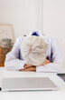 © Xavier Lorenzo - Exhausted senior doctor in a white coat taking a break while sitting on desk at medical office. Healthcare and medicine concept