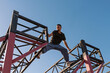 © Vagengeim - An athletic man stretches his body between two steel beams during an intense parkour maneuver at a specialized urban training structure in full daylight