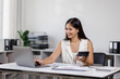 © David - Asian female Using laptop computer and working at office with calculator document on desk, doing planning analyzing the financial report, business plan investment, finance analysis concept.