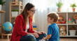 © Pete - Speech therapist smiles talking to young boy in brightly lit room. Child learns, speaks, listens during therapy session. Educational toys, globe visible in background.
