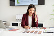 © Fahng - Designer working in office and making call on mobile phone. Female interior designer talking by mobile phone at desk in office.