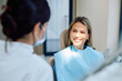 © we.bond.creations - Young woman sitting in a dental chair smiling at a dentist, discussing her oral hygiene and receiving a checkup